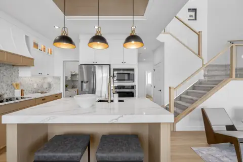 Kitchen with a quartz island, pendant lights and a glass-railed stair — a finished Vita home in Triomphe Estates. Furniture and décor are staging for the photos.