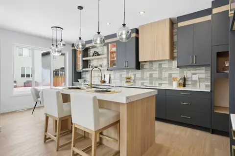 Kitchen with a wood-tone island, two-tone cabinets and glass pendants — the second Vita home. Furniture and décor are staging for the photos.